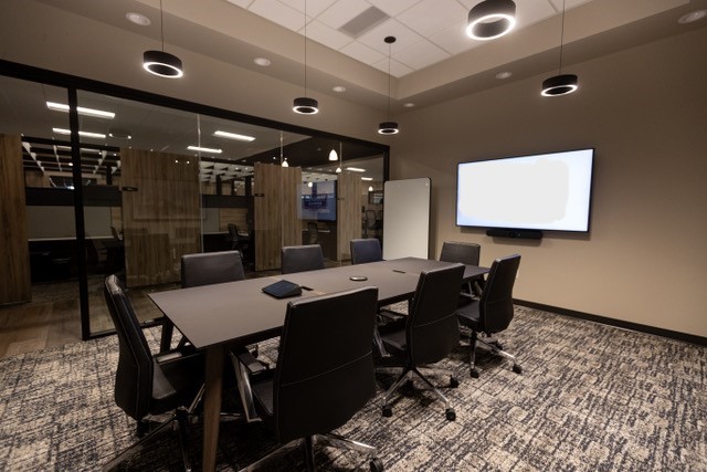 Photo of a conference room with a glass wall, 8 chairs and a TV screen on the wall.